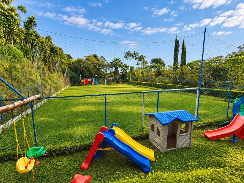 Campo de futebol gramado com alambrado azul e playground infantil em primeiro plano